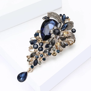 Elegant deep blue crystal brooch with teardrop pendant on a white geometric stand
