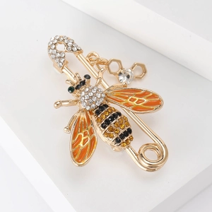 Détail de broche abeille avec ailes émaillées, strass et pendentif alvéolé sur fond blanc
