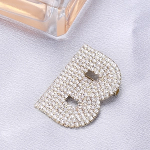Élégante broche lettre B dorée avec strass scintillants sur fond de soie