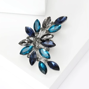 Artistic crystal brooch with navy blue leaf-shaped gems on white geometric podium