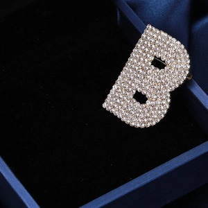 Détail d'une broche lettre B argentée sertie de strass sur un tissu en soie bleue