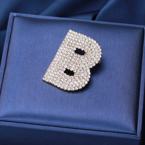 Détail macro de la broche dorée lettre B avec strass étincelants sur velours bleu