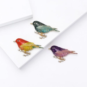 Three colorful enamel bird brooches on crystal branches displayed on a white stand