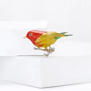 Close-up of colorful enamel bird brooch on gold branch with sparkling rhinestones