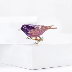Elegant purple and pink enamel bird brooch with crystals on a minimalist display