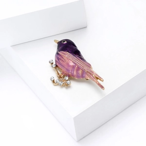 Macro shot of purple gradient oil bird brooch with sparkling rhinestones on golden branch