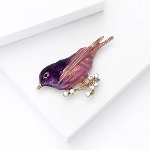 Detailed macro of bird brooch featuring purple enamel wings and rhinestone branch