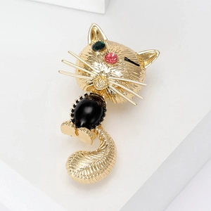 Détail d'une broche chat dorée avec yeux en strass verts et corps en résine noire
