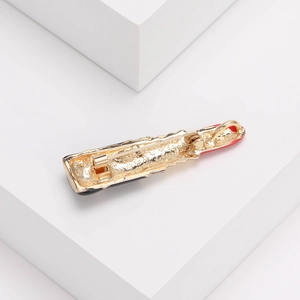 Vue détaillée du dos d'une broche rouge à lèvres dorée avec épingle de sûreté et émail