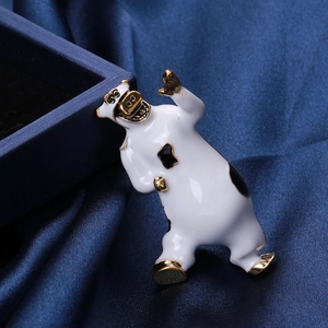 Dettaglio macro di una spilla a forma di mucca in smalto bianco con finiture in oro su seta