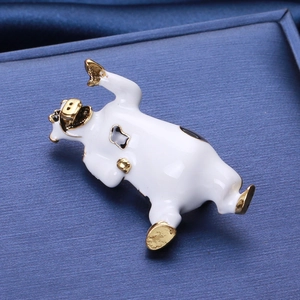 Dettaglio della spilla a forma di mucca in smalto bianco con accenti in metallo dorato