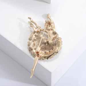 Broche ballerine dorée élégante avec épingle de sécurité sur un support blanc minimaliste