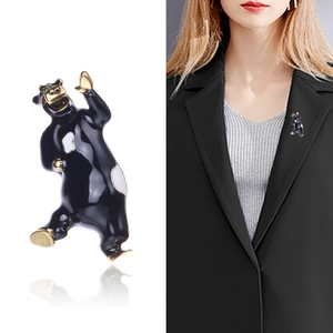 Spilla a forma di orso in smalto nero con bordi dorati mostrata su sfondo e su un blazer