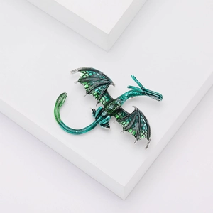 Détail d'une broche dragon en émail bleu et vert sur un support géométrique blanc
