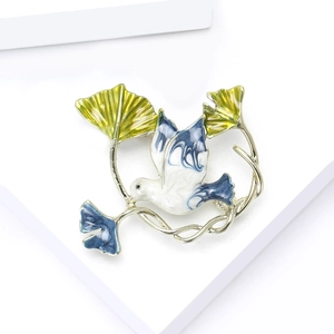 Elegant enamel peace dove brooch with ginkgo leaves and blue wings on a white stand