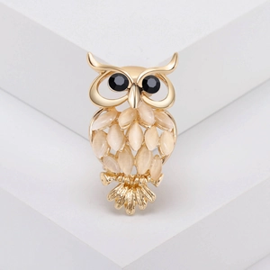 Gros plan détaillé d'une broche hibou dorée avec pierres œil-de-chat sur socle blanc