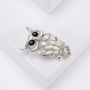Détail macro de broche hibou avec plumes en opale blanche et yeux en pierres noires sur métal