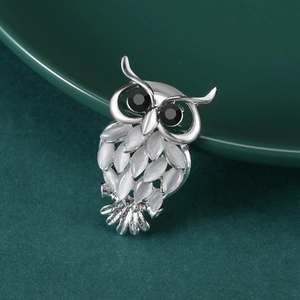 Vue macro de broche hibou argentée avec opales blanches sur fond vert foncé