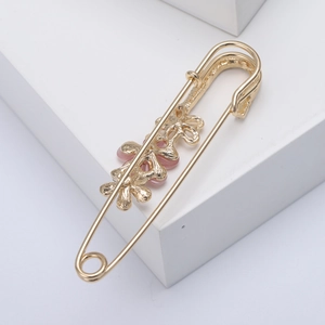 Detailed view of a gold safety pin brooch featuring delicate pink floral embellishments