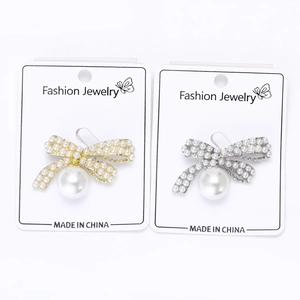 Detailed view of silver and gold bow brooches featuring white pearl inlays and large pendants