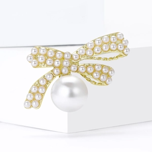 Elegant gold bow brooch with multiple pearls on a white geometric display stand