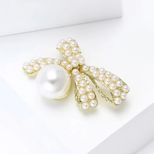 Detailed close-up of golden bow brooch featuring dense pearl pavé and a large accent pearl
