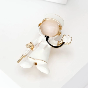 Cartoon doctor brooch with pink cat eye stone and gold syringe pin on white stand