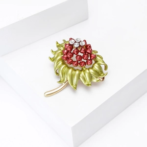 Dettaglio della spilla a fiore di melograno smaltata con bacche rosse e strass lucidi