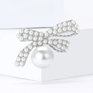 Elegant silver bow brooch with white pearls on a minimalist white platform