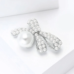 Detail of elegant silver bow brooch featuring lustrous white pearls on a white prop