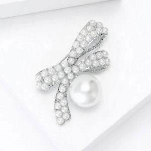 Detail of silver bow brooch with white pearls on a geometric white block background