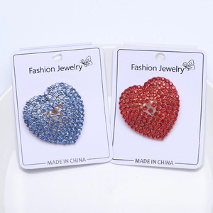 Close-up of heart-shaped brooches set with red and blue rhinestones on a white display