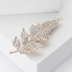 Élégante broche en forme de feuille or rose et cristaux sur présentoir géométrique blanc