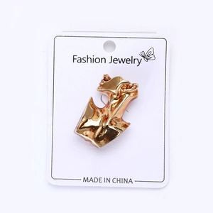 Detailed view of an abstract gold human figure brooch with a polished finish on white card