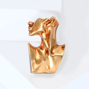 Abstract portrait sculpture brooch in mirror gold finish on a minimalist white platform