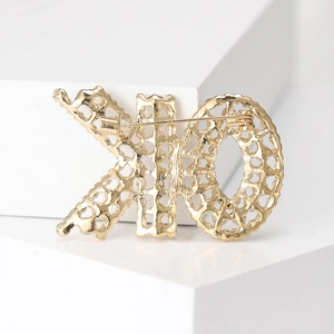 Broche XO dorée en maille ajourée avec épingle de sûreté sur fond blanc géométrique