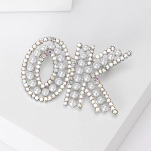 Détail macro de la broche perle en forme de OK avec métal argenté et strass