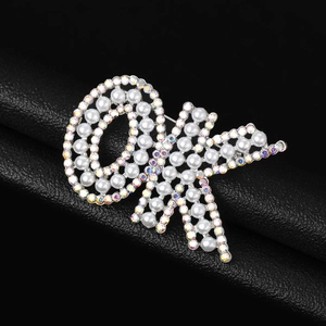 Gros plan d'une broche geste OK en métal argenté avec strass colorés et perles