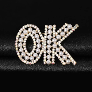 Vue macro de la broche lettre OK ornée de perles blanches et strass sur cuir noir texturé