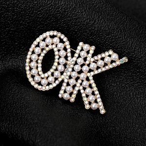 Détail macro d'une broche dorée avec perles blanches et strass colorés sur cuir noir