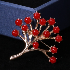 Détail d'une broche feuille dorée avec perles rouges sur velours noir