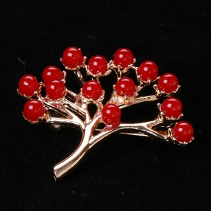 Vue détaillée d'une broche arbre dorée avec perles rouges sur fond de velours noir