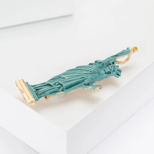 Green enamel Statue of Liberty brooch with gold metal base on a white display stand