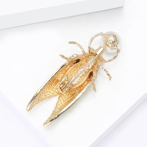 Détail de l'arrière d'une broche cigale dorée avec épingle de sûreté et perle