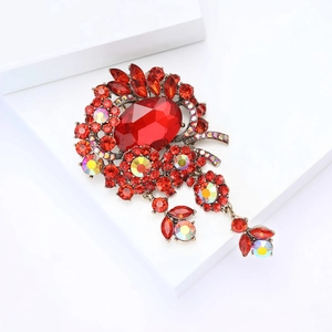 Detailed close-up of a glamorous red crystal floral brooch with tassel on a white stand