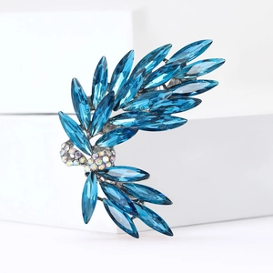 Elegant silver bow brooch with blue crystal feathers on a white minimalist block