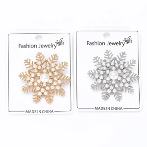 Detailed close-up of gold and silver snowflake brooches with white pearls set on display card