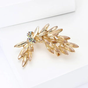 Close-up of champagne crystal leaf brooch with gold metal base and sparkling rhinestones