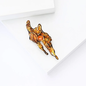 Artistic amber lava brooch with gold metal edge displayed on a minimalist white stand
