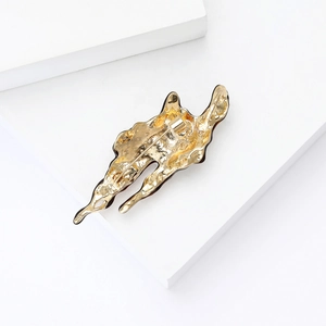 Detail of gold enamel lava brooch with abstract irregular melting metal texture on a white block